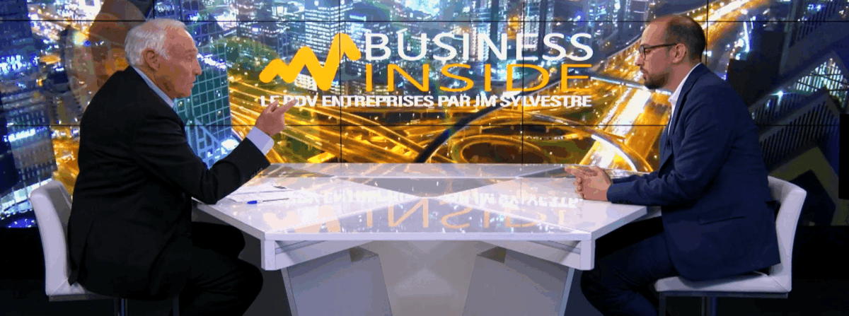 Two men sitting at a table on the plateau of Business Insider TV talking to each other.