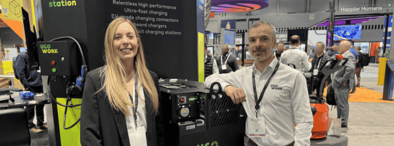 Two smiling UgoWork team members standing next to a UgoWork lithium-ion battery on display at the ProMat trade show.