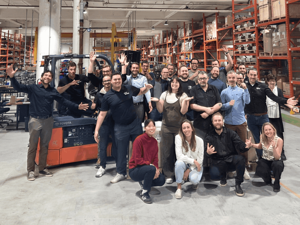UgoWork team gathered in the warehouse, smiling together in front of a forklift powered by a lithium-ion battery.