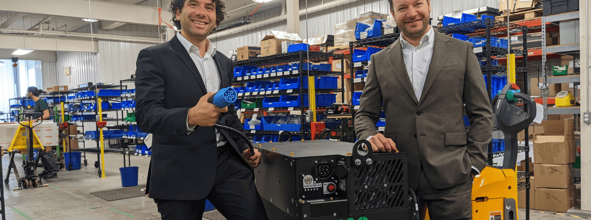 Two men posing in a factory standing around a UgoWork lithium-ion battery on a forklift