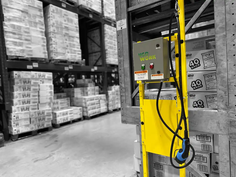 Station de recharge compacte avec connecteur de type EV pour chariots élévateurs installée au bout d'une allée dans un entrepôt.