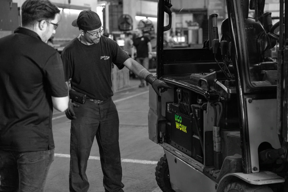 Lift truck operator with technician looking at lithium-ion battery in a sit-down counterbalanced forklift.